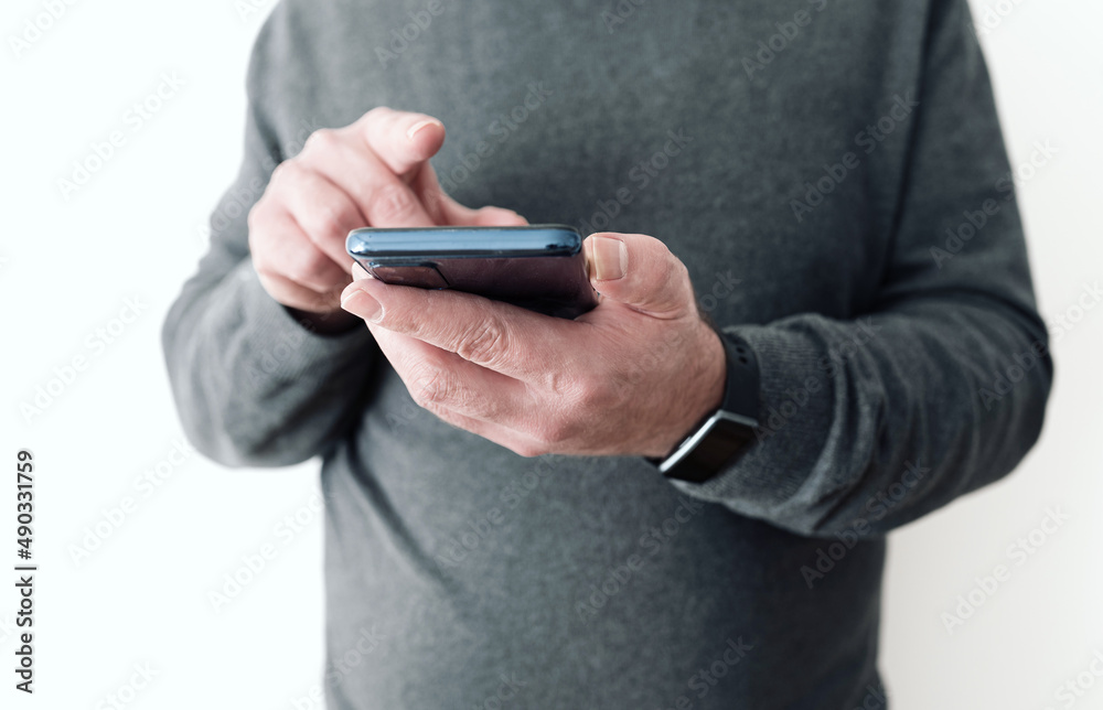 midsection of man holding smartphone in hand in front of white wall midsection of man holding smartphone in hand in front of white wall
