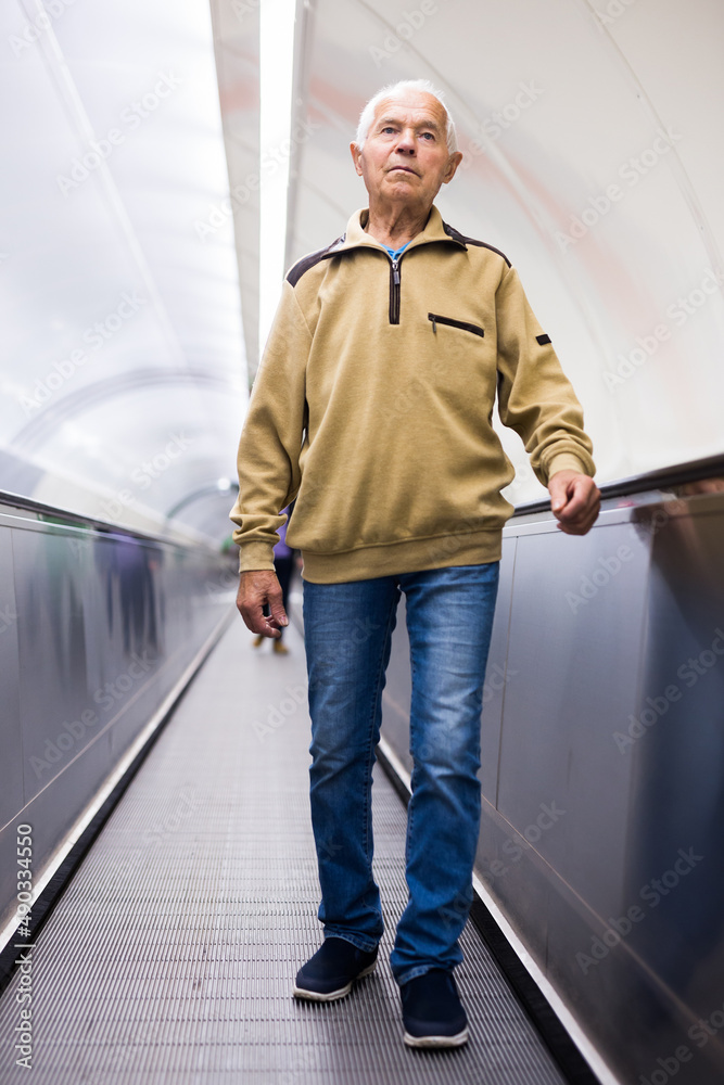 Senior man walks down the travelator to subway station platform