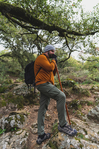 Chico alto con barba con ropa deportiva realizando senderismo por ruta verde en la sauceda con un palo de caminar