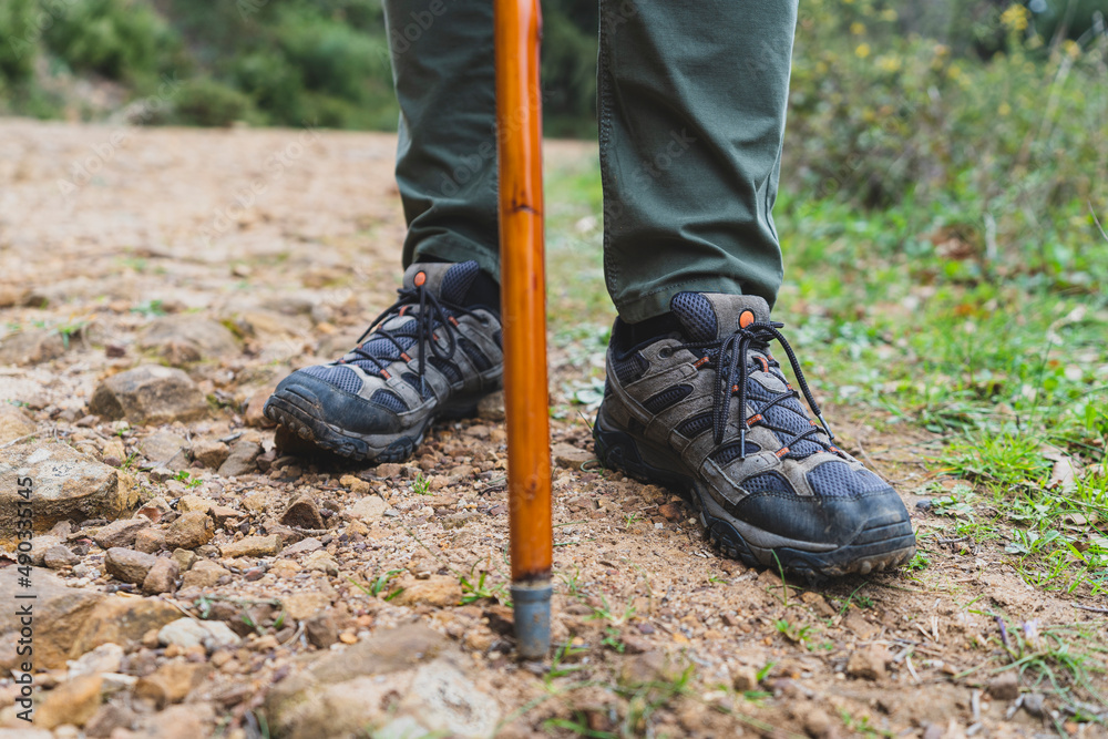 Detalle de los pies de un senderista con un palo de ayuda en un camino de montaña