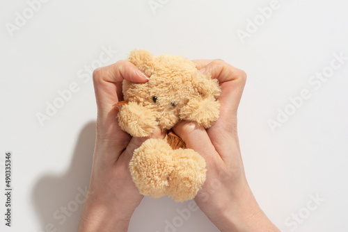 Hand holding squashed teddy bear toy isolated on white background. Concept of a friend and love. A mother holds a small brown toy bear on a palm isolated.	
