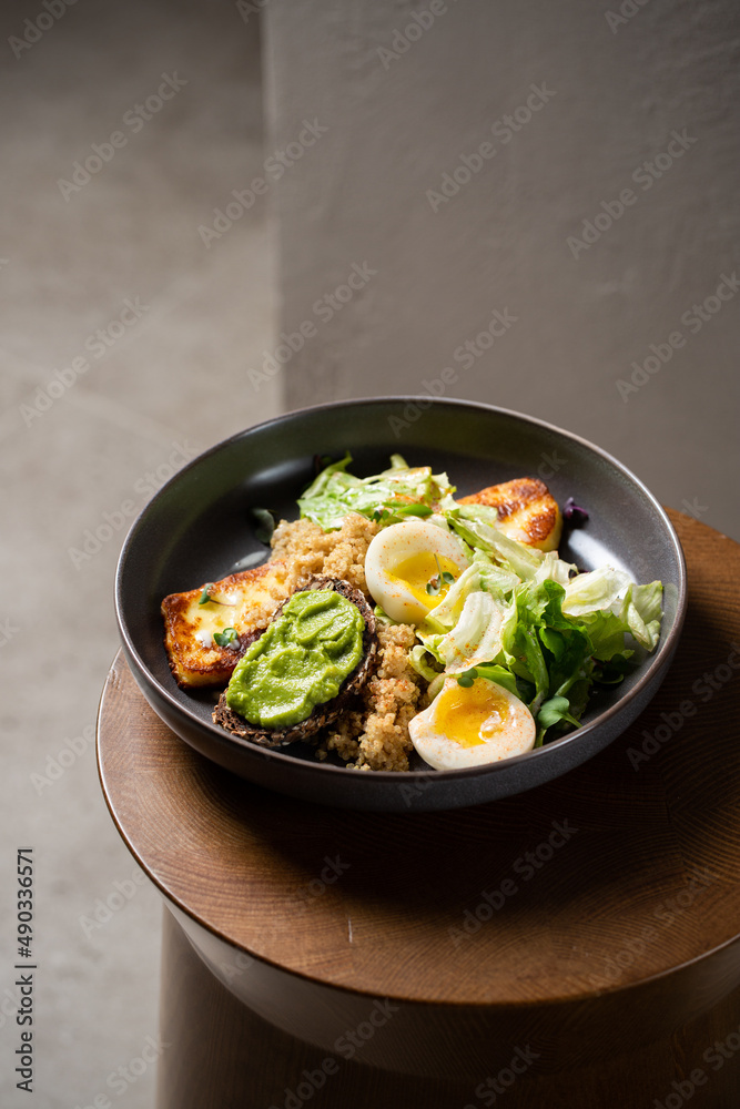 Plate with breakfast salads: avocado toast, egg, greens, fried cheese, quinoa Plate with breakfast salads: avocado toast, egg, greens, fried cheese, quinoa