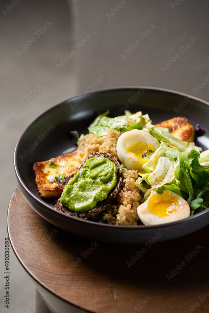 Plate with breakfast salads: avocado toast, egg, greens, fried cheese, quinoa Plate with breakfast salads: avocado toast, egg, greens, fried cheese, quinoa