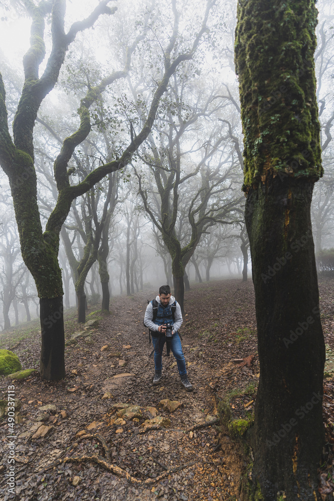 Chico con equipo de senderismo haciendo una foto en medio del camino de un bosque lleno de niebla Chico con equipo de senderismo haciendo una foto en medio del camino de un bosque lleno de niebla