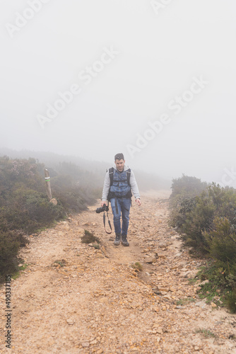 Chico joven bajito andando por camino de piedra rodeado de niebla y tomando fotos