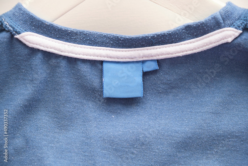 Blank white laundry care clothes label on blue fabric texture background.