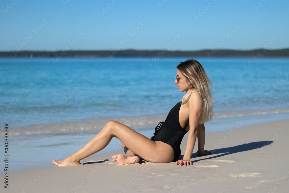 portrait of young woman in black bikini sitting on the beach
