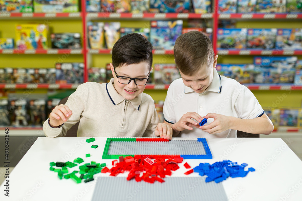 Fototapeta premium Children play in the designer at the table. Two boys play together with colored plastic blocks in the gaming center, school.