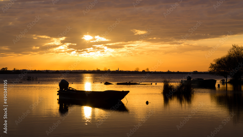 Barque de pêche sur un lac calme au soleil couchant à contre-jour, avec reflets, dans les teintes chaudes. Lac de Grand-Lieu près de Nantes