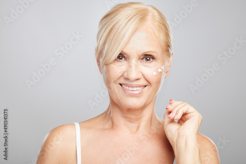 An attractive blond senior woman putting anti-age creme. Beauty photography