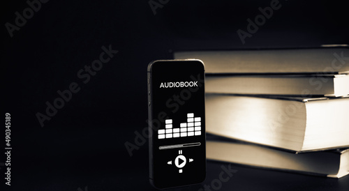 Audio listen book. Phone screen with audiobook app on paper books black background. Online education course, E learning class and e book digital technology concept.