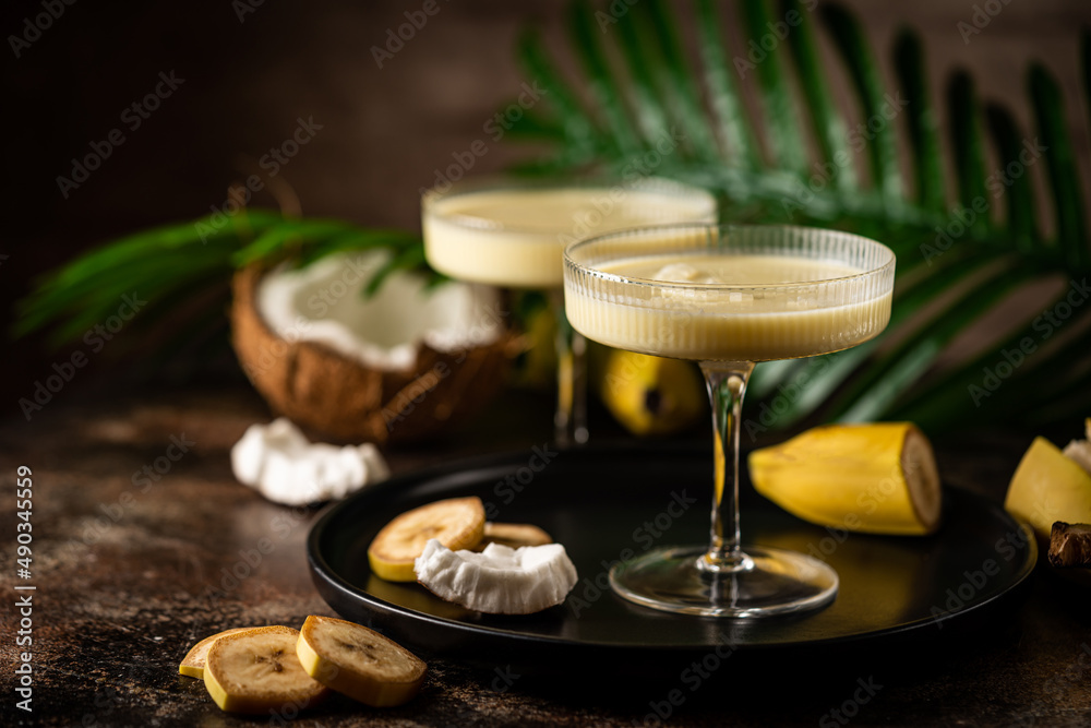 banana cocktail with coconut milk in a glass on dark background with palm leaves banana cocktail with coconut milk in a glass on dark background with palm leaves
