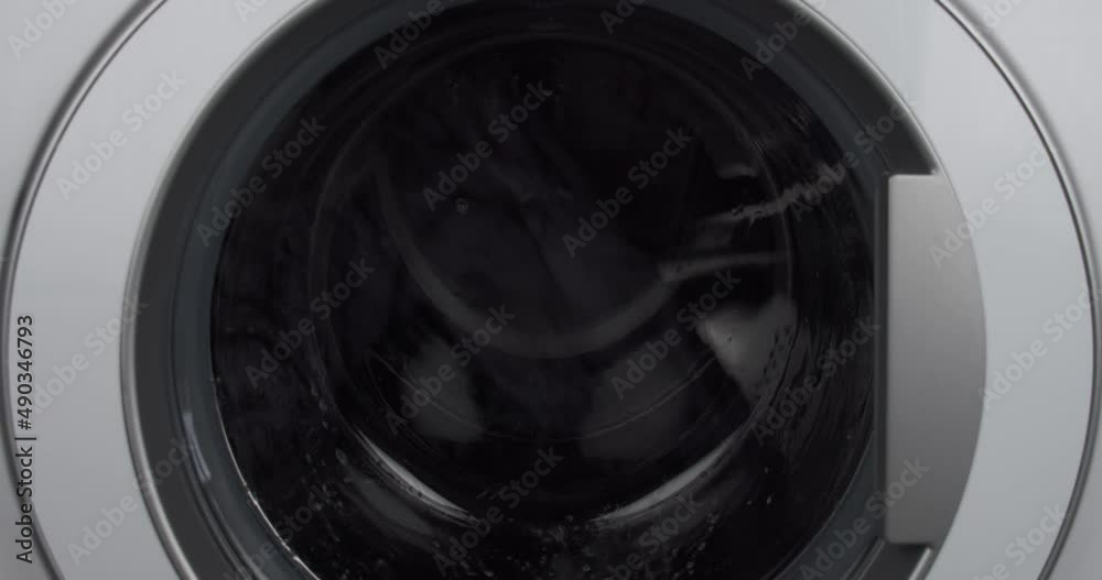 Close up static shot of washing machine washing dark clothes Close up static shot of washing machine washing dark clothes