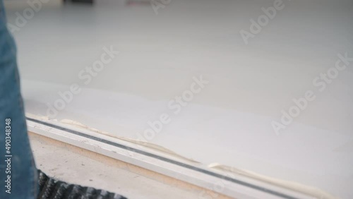 Construction worker performs floor screed indoors. Self-priming freshly prepared floor. 4K