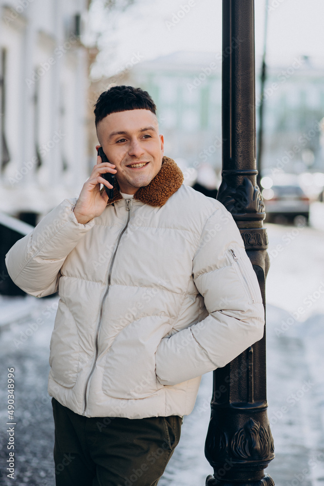 Young man in winter jacket using phone outside the street Young man in winter jacket using phone outside the street