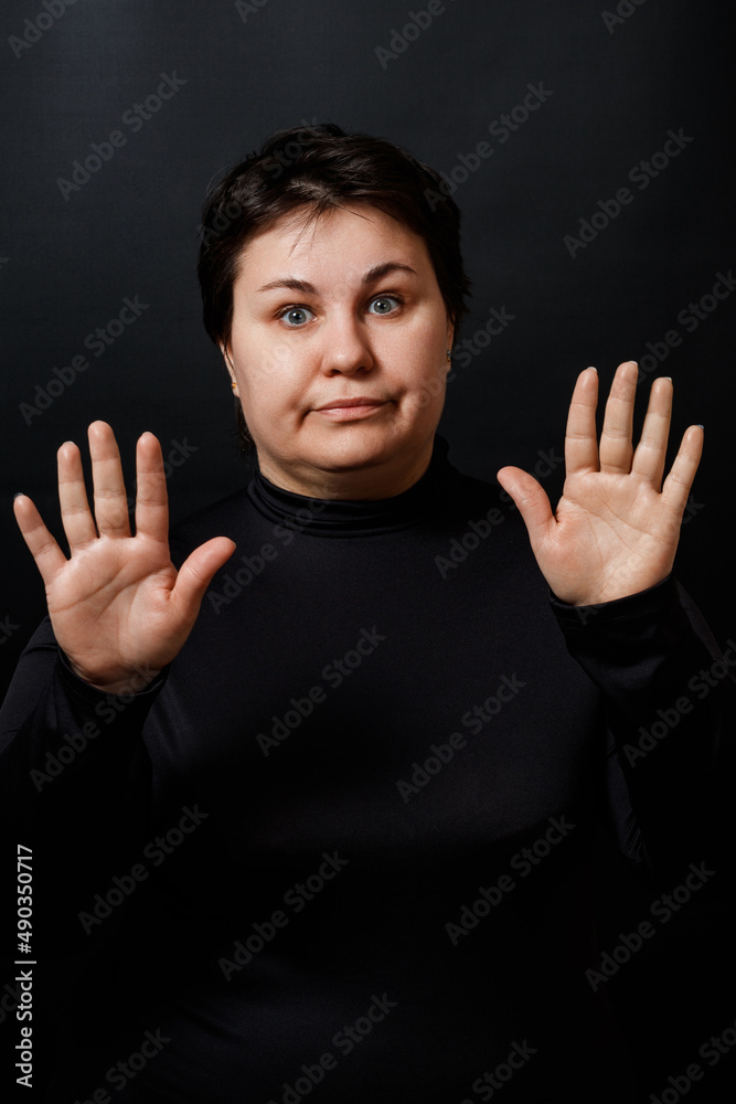 brunette woman stretches her palms forward on a black background. stop gesture brunette woman stretches her palms forward on a black background. stop gesture