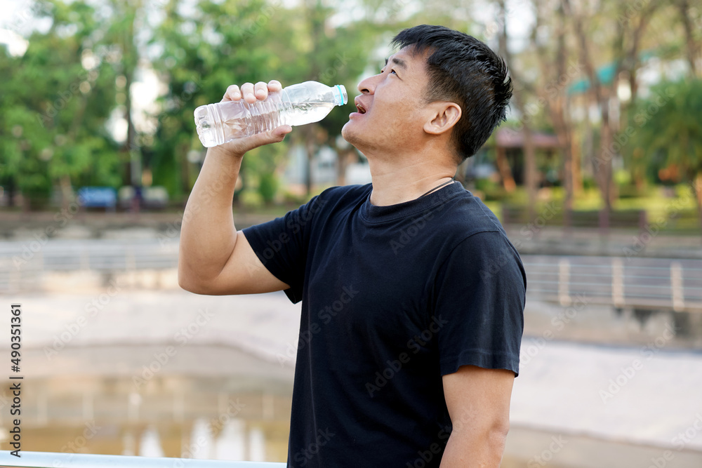 Portrait of Asian man is drinking water from bottle at the outdoor park. Concept : Healthy lifestyle. Drink water for health. Portrait of Asian man is drinking water from bottle at the outdoor park. Concept : Healthy lifestyle. Drink water for health.