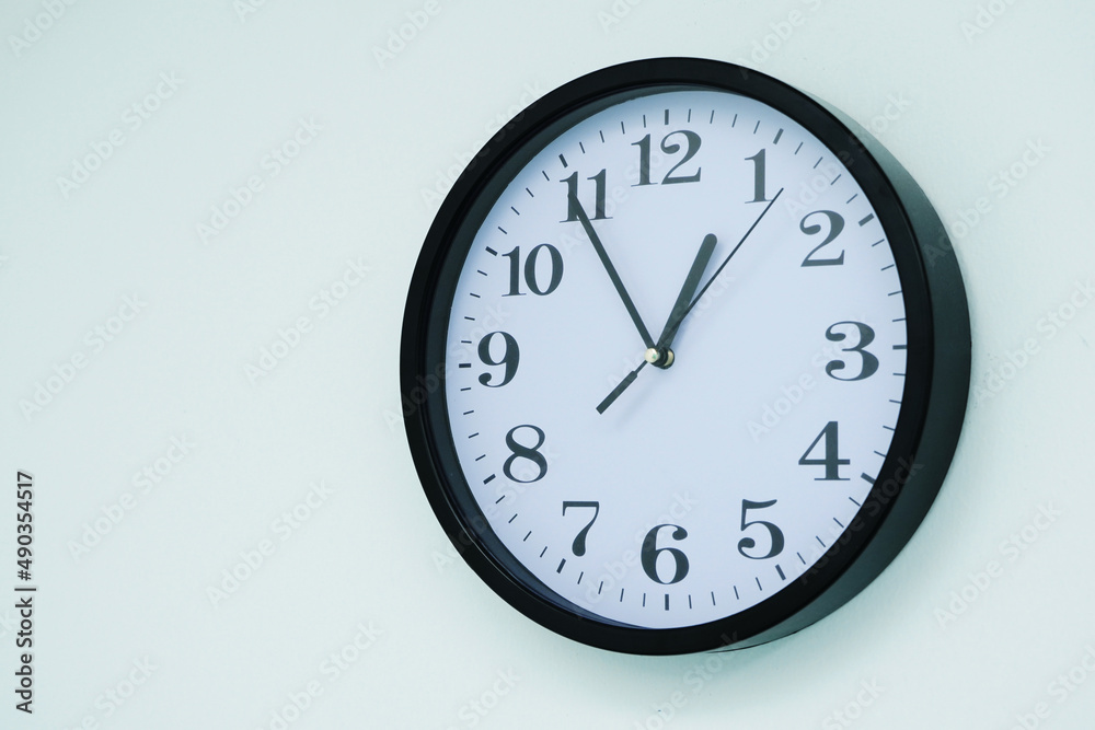 Wall clock, white with black border, telling time fifty-five minutes noon. Wall clock, white with black border, telling time fifty-five minutes noon.