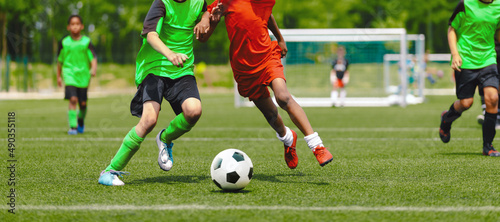 Horizontal image of teenagers playing football. Happy boys kicking classic soccer ball on grass field. School children compete in sports game on training pitch