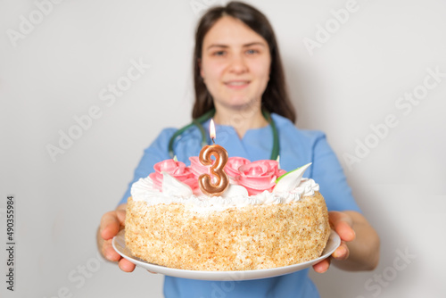 The doctor or nurse holds a birthday cake with the number three for the anniversary of the opening of the clinic