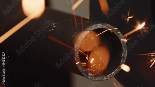 Metal pipe is sawed using an angle grinder and cutting disc, sparks fly out, closeup. Hollow metal pipe is cut with construction tool