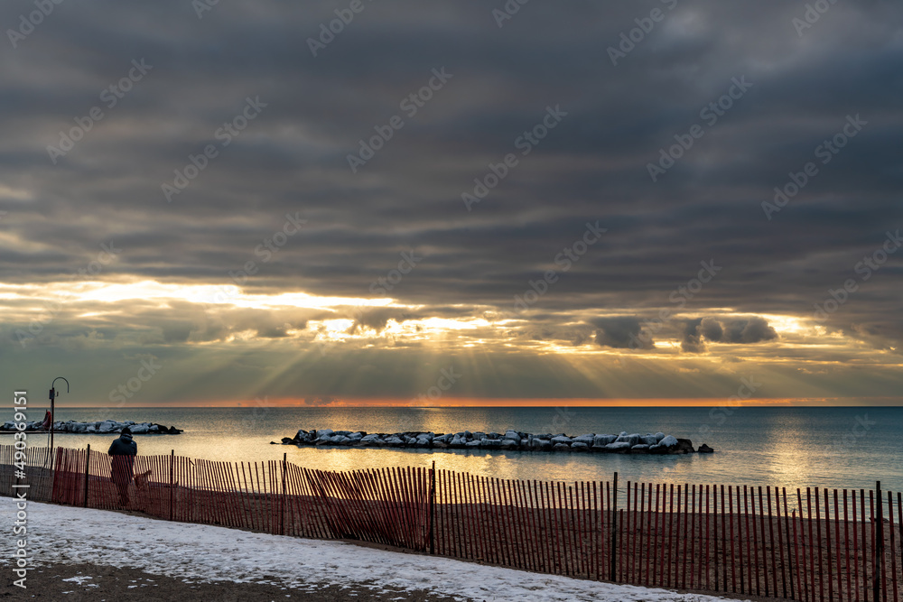 Obraz premium A woman and her dog walk on an empty beach just after dawn on a March morning in Toronto's Beaches neighbourhood. Room for text.