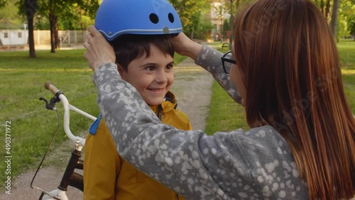mother puts on safety helmet on sons head. preparing to ride a bicycle