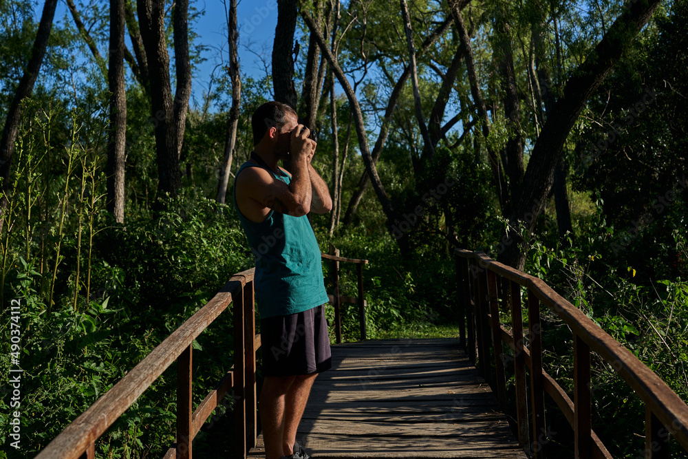 Naklejka premium young man photographing in nature with vintage camera