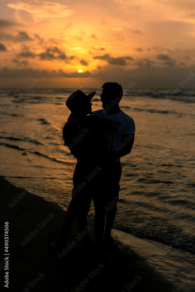 Young latin couple hugging each other on the beach at sunset