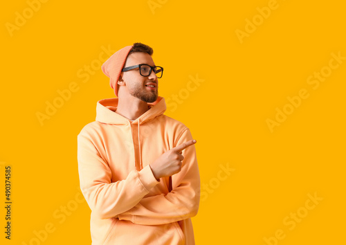 Young guy in stylish hoodie pointing at something on color background © Pixel-Shot