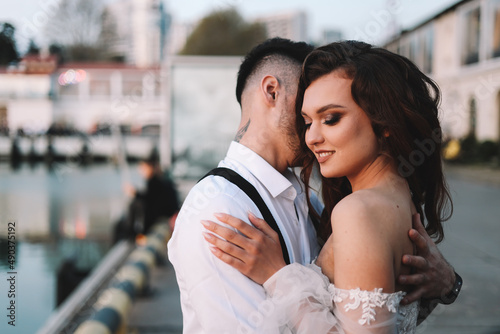 Happy lovers, the bride and groom in elegant wedding dresses go on a honeymoon by sea on yacht in the marina in Sochi in summer outdoor. Off-site chamber wedding ceremony for a married couple in love