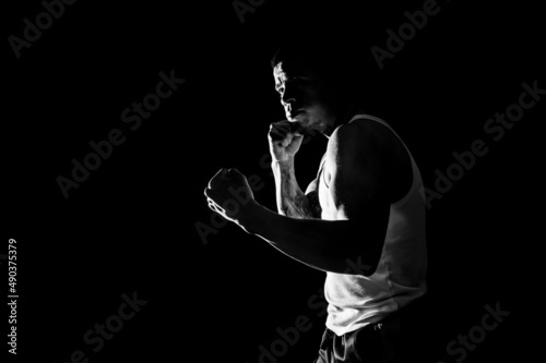 Young man practicing shadow boxing over black background. Black and white high contrast image. Strenght and motivation.
