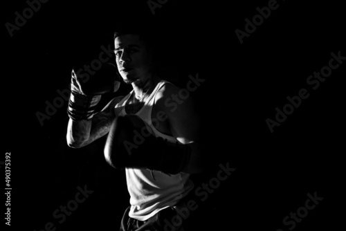 Young man practicing shadow boxing over black background. Black and white high contrast image. Strenght and motivation.