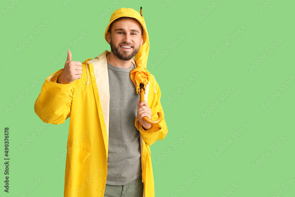 Young man in stylish raincoat and with umbrella showing thumb-up gesture on color background Young man in stylish raincoat and with umbrella showing thumb-up gesture on color background