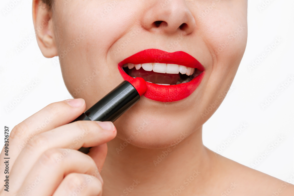 Cropped shot of a young beautiful caucasian woman applying a bright red color lipstick on her lips isolated on a white background. Close-up, make up