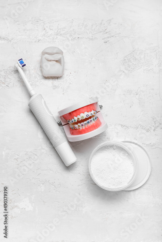 Model of jaw with braces, toothbrush, powder and dental floss on light background