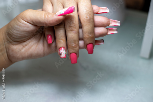 Manicurist performing the process of applying red acrylic nails with flower decorations  in a beauty salon