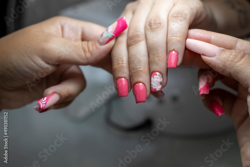 Manicurist performing the process of applying red acrylic nails with flower decorations, in a beauty salon
