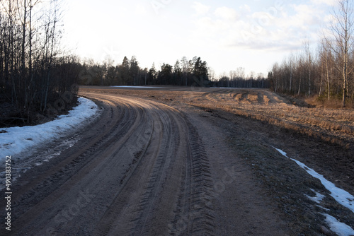 winding sand and gravel dirt road in Latvia countryside  melting snow on roadsides