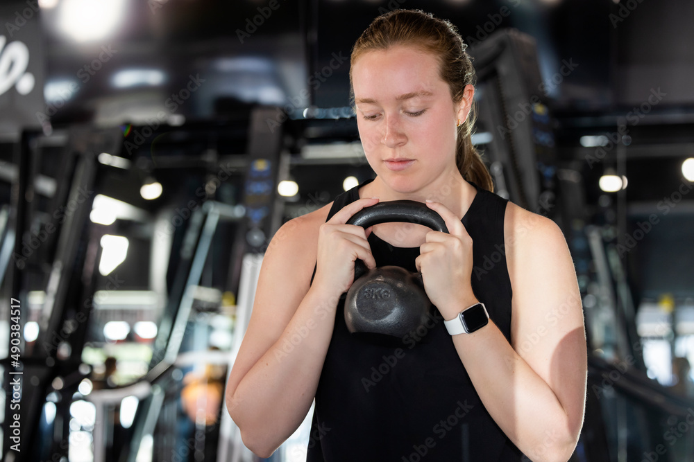 Woman in gym holding dumbbell doing squats Woman in gym holding dumbbell doing squats