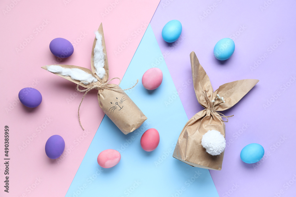 Composition with Easter bunny gift bags and  eggs on color background