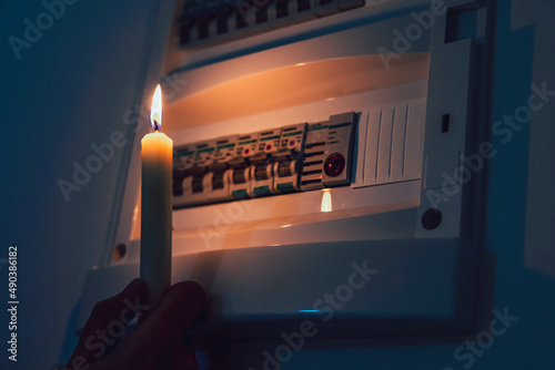 Energy crisis. Hand in complete darkness holding a candle to investigate a home fuse box during a power outage. Blackout concept. photo