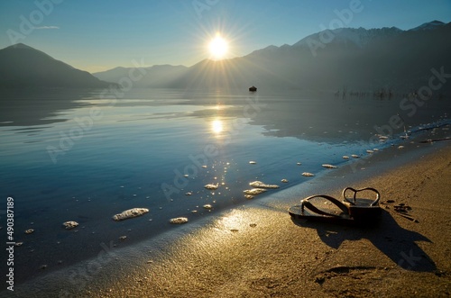 Flip Flops on the Sand Beach on Alpine Lake Maggiore with Sunlight and Mountain in Ascona, Switzerland. photo