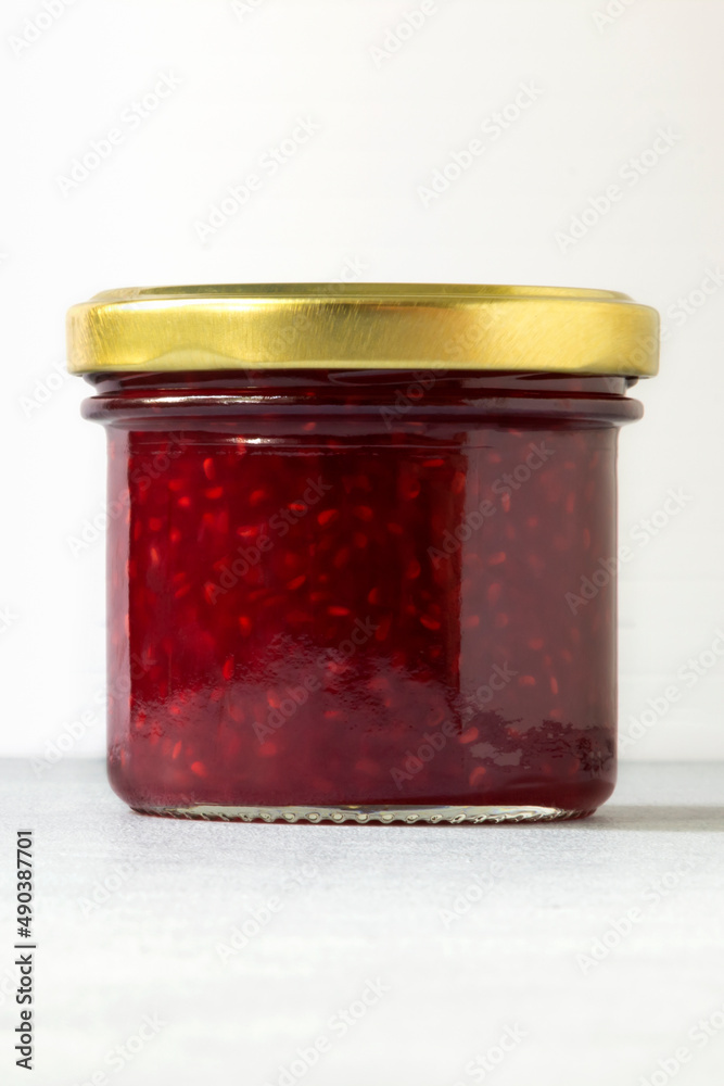 Packaging for jam. Raspberry jam in glass jar close-up on white background. Vertical layout. Packaging for jam. Raspberry jam in glass jar close-up on white background. Vertical layout.
