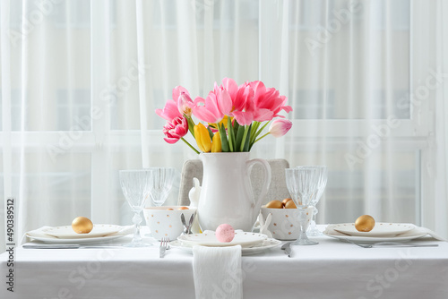 Beautiful table setting with Easter eggs and tulips in room