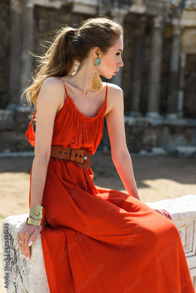 A young adult girl in a red dress on the background of the ruins of an ancient temple. Fashion stylish portrait