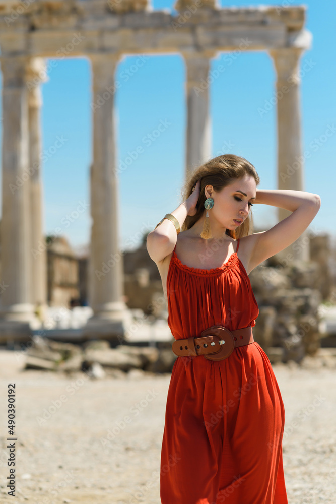 A young adult girl in a red dress on the background of the ruins of an ancient temple. Fashion stylish portrait