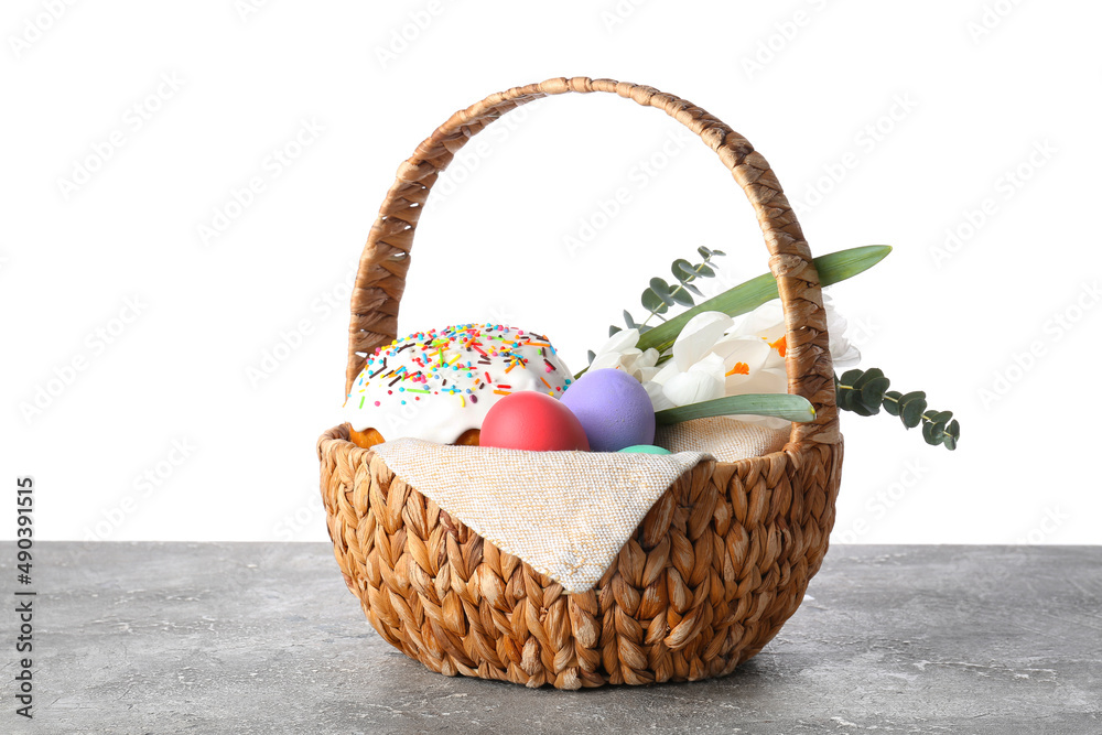 Gift basket with painted Easter eggs, flowers and cake on table against white background Gift basket with painted Easter eggs, flowers and cake on table against white background