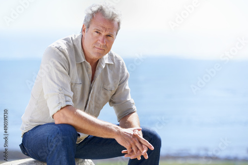 Years of rugged experience are reflected in his face. Portrait of a mature man sitting outdoors.