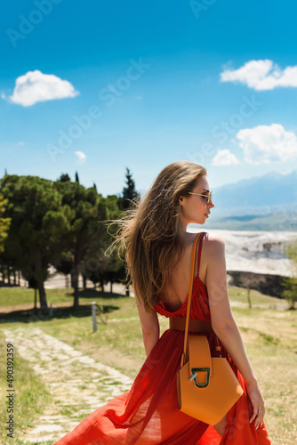 A young beautiful woman in a red dress walking in Pamukkale, Turkey, against the backdrop of the ruins of the ancient city of Hierapolis © ANR Production